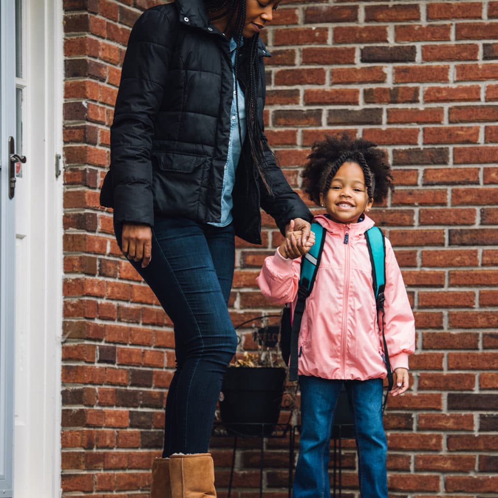 Little girl smiles with her parent with backpack on