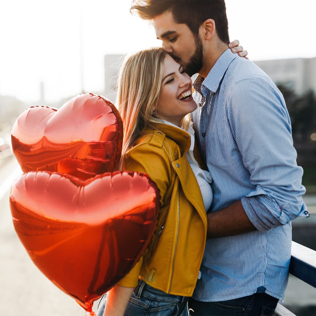 Photo of a couple holding red heart-shaped balloons