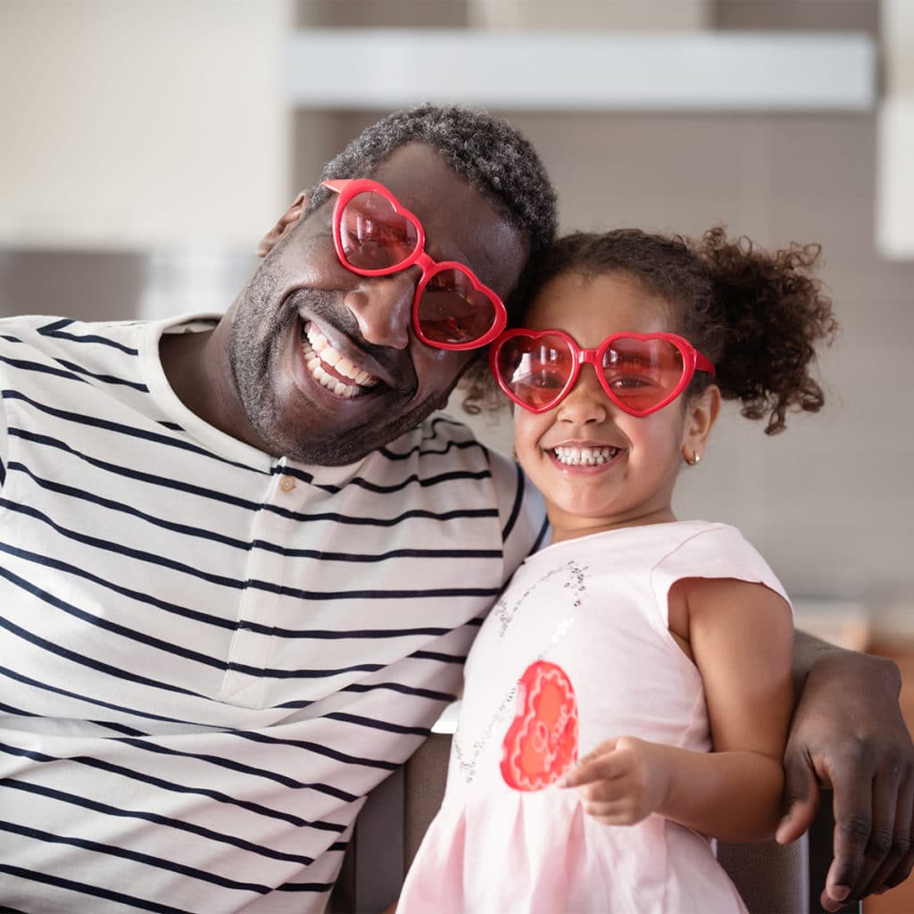 Man and little girl celebrating Valentine's Day, wearing red heart-shaped sunglasses