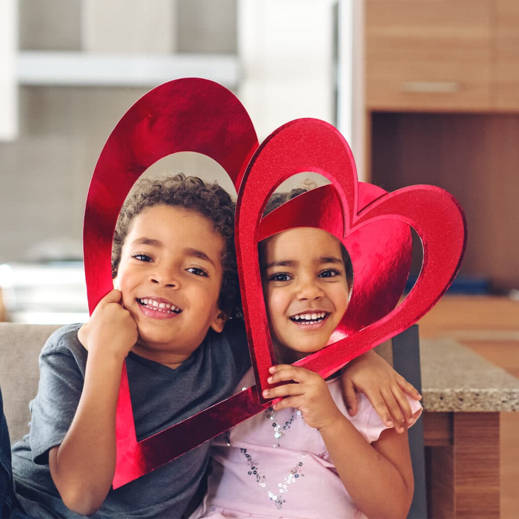 Two smiling kids holding up shiny red hearts for Valentine's Day