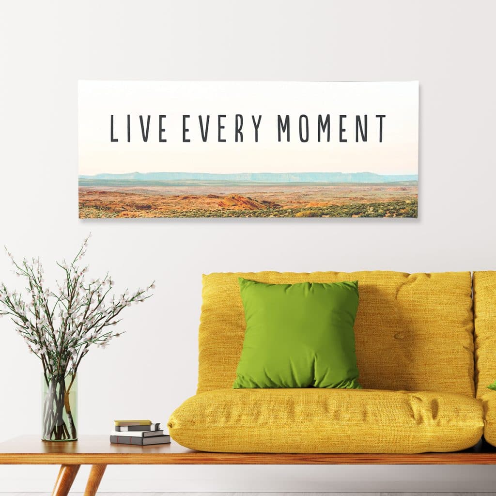 Panoramic canvas print that reads "Live every moment" hanging over a yellow couch