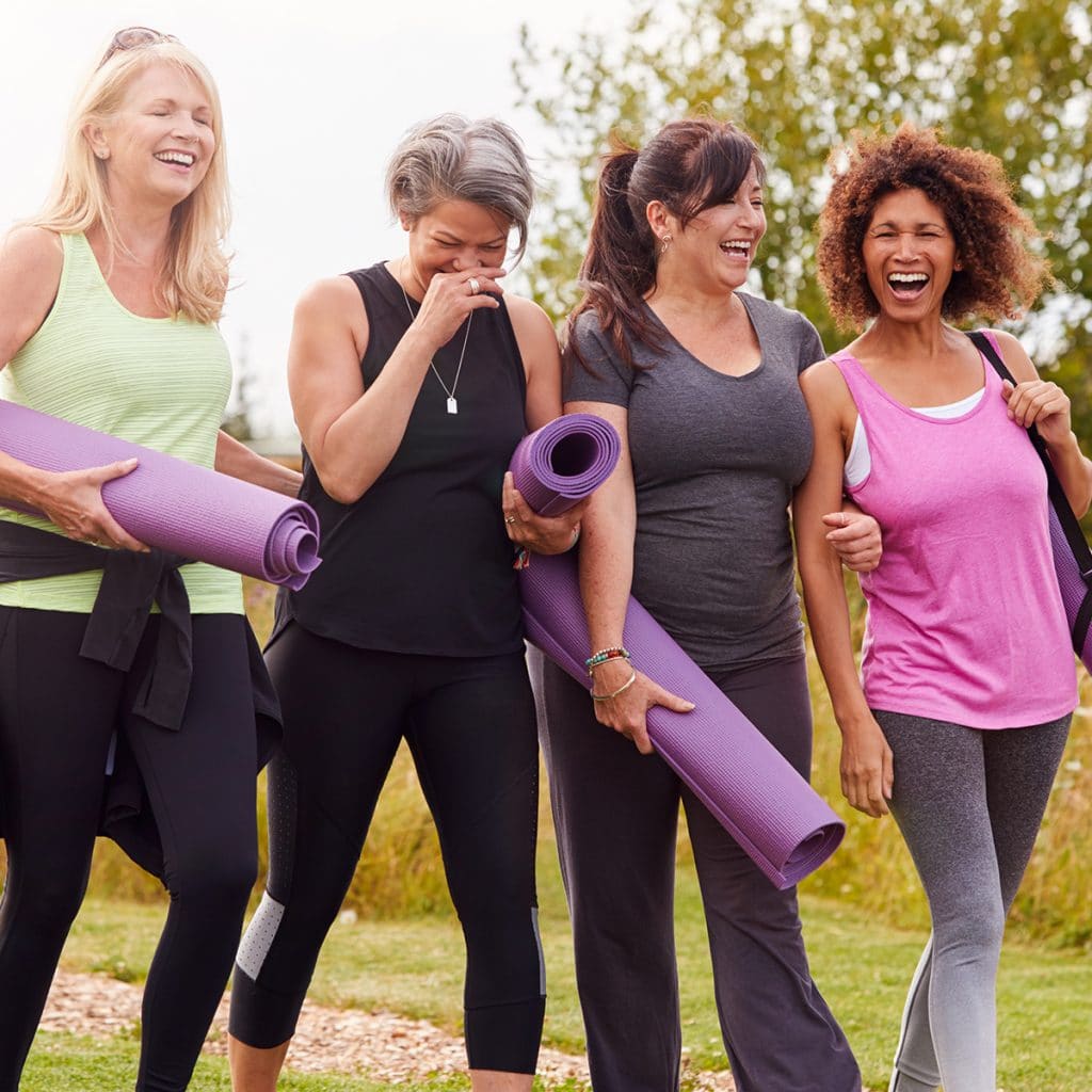 Four women in workout attire walking together holding yoga mats