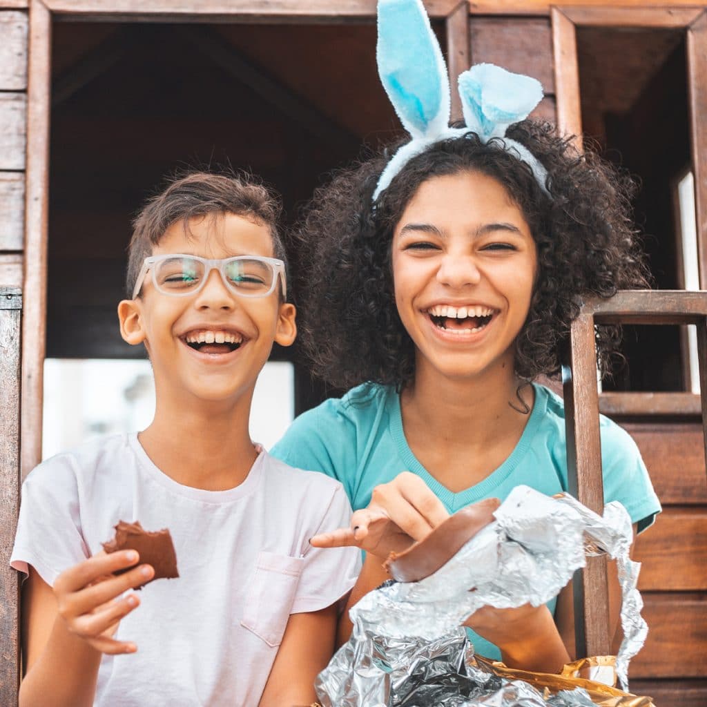 Two kids laughing and smiling while eating chocolate and wearing Easter bunny ears