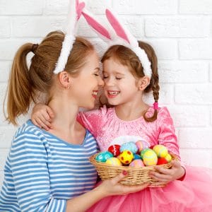 Mom and daughter smiling, wearing bunny ears, and holding a basket of Easter eggs