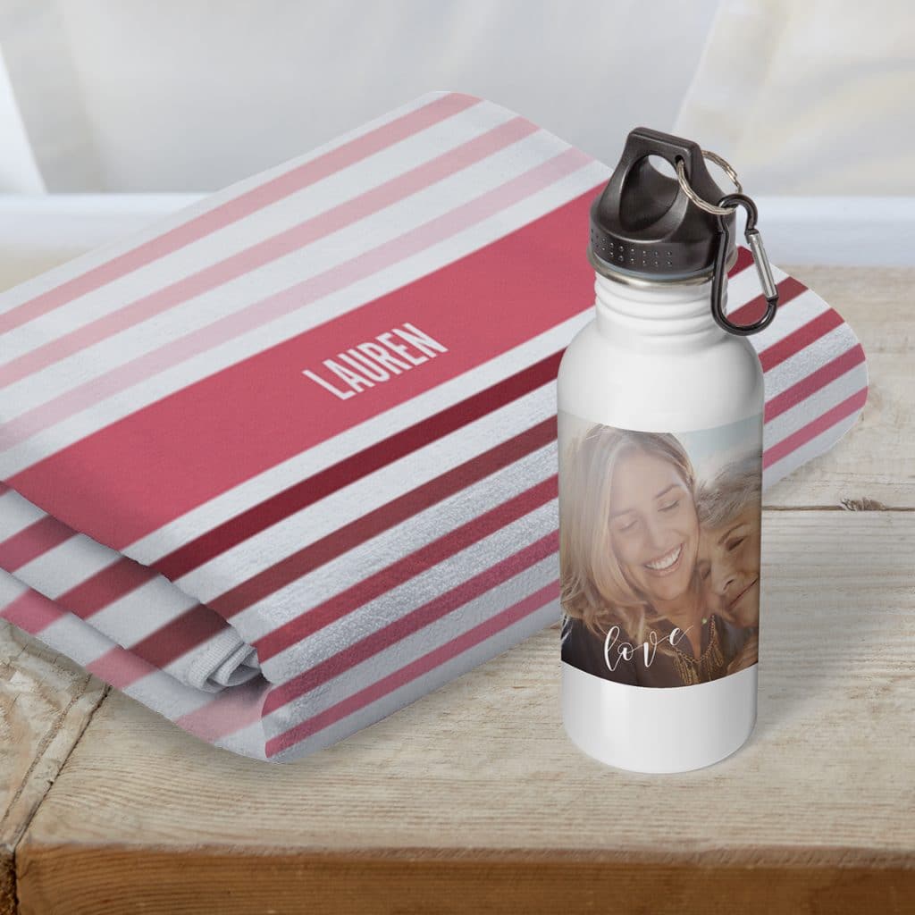 A customized beach towel with the name Lauren folded behind an insulated water bottle featuring a sweet photo of mother and grown daughter