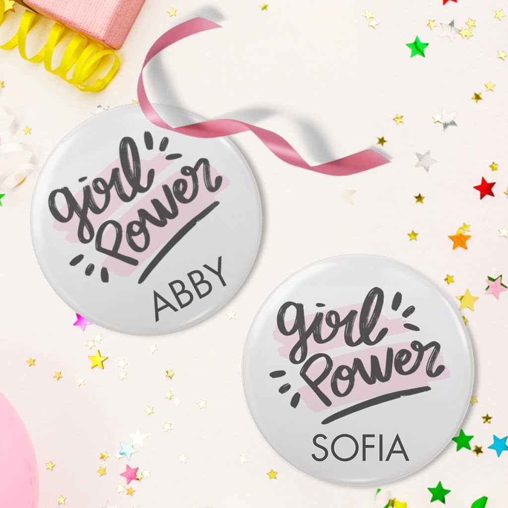 Two "Girl Power" button pin designs with the names Sofia and Abby laying on a table surrounded by star confetti