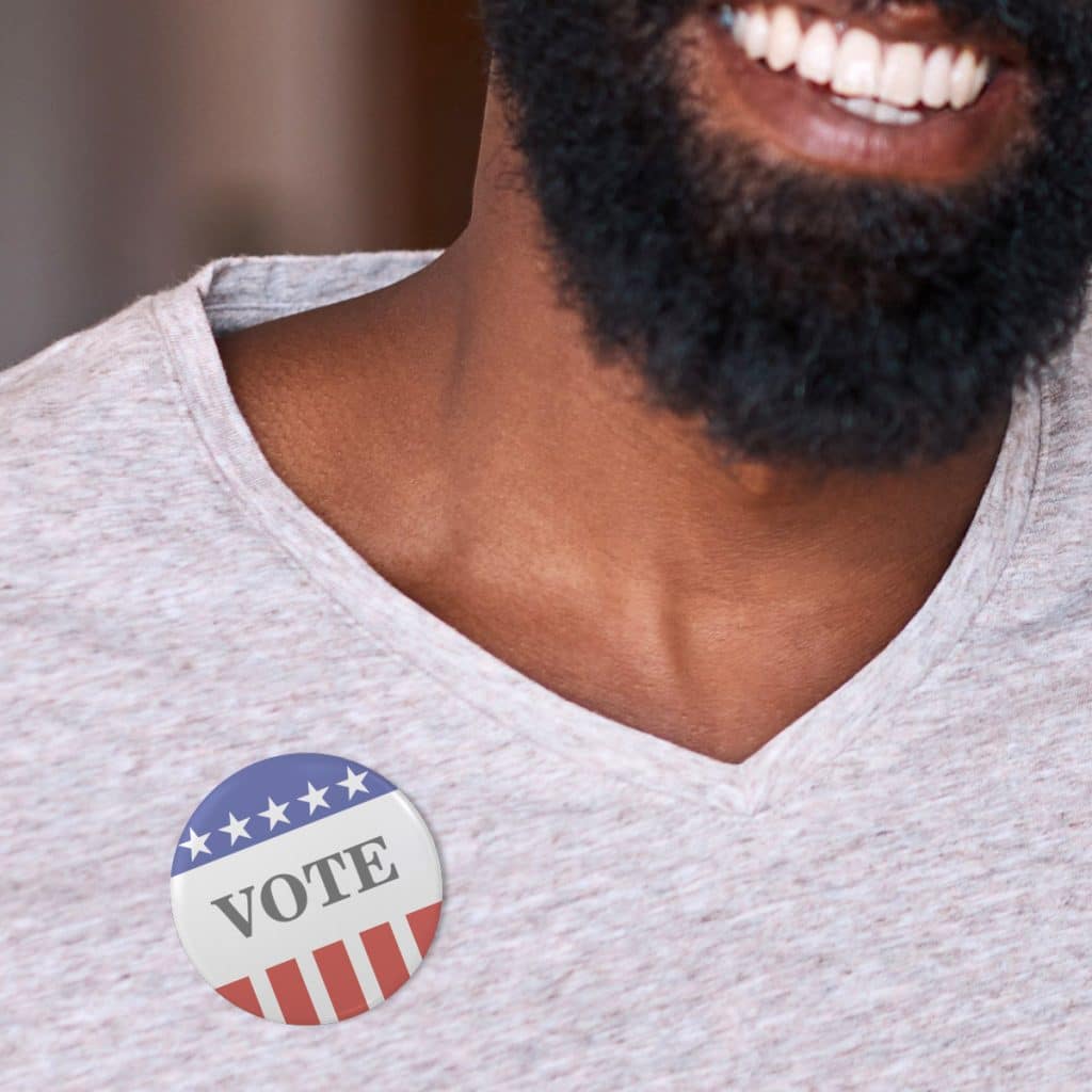 Photo of a man smiling wearing a VOTE pin