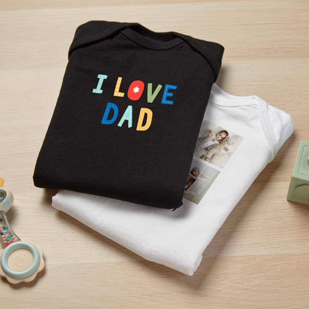 Image of two baby bodysuits. One in black that reads "I LOVE DAD" and one in white with a baby photo collage.