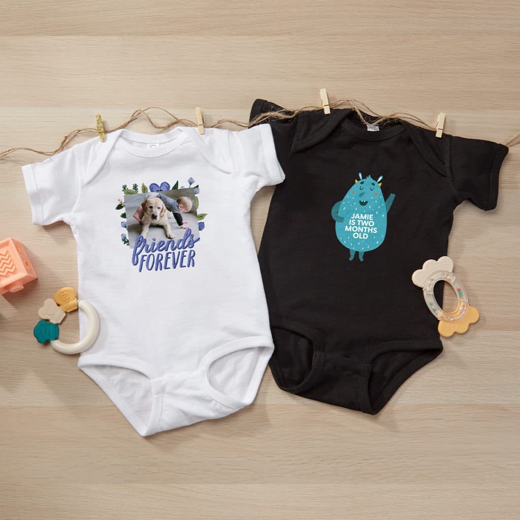Flat lay image of one white baby bodysuit and one black baby bodysuit, each featuring a different design.