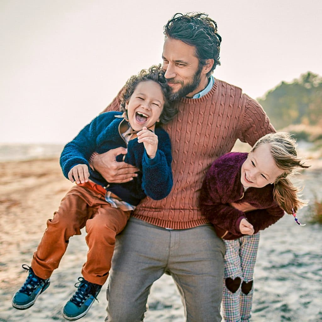 Sweet family photo of dad holding his son and daughter, laughing, on the beach