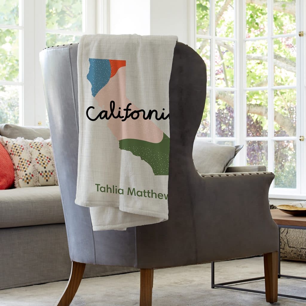 Image of a blanket draped over the back of a chair. The blanket features an illustration of the state of California.
