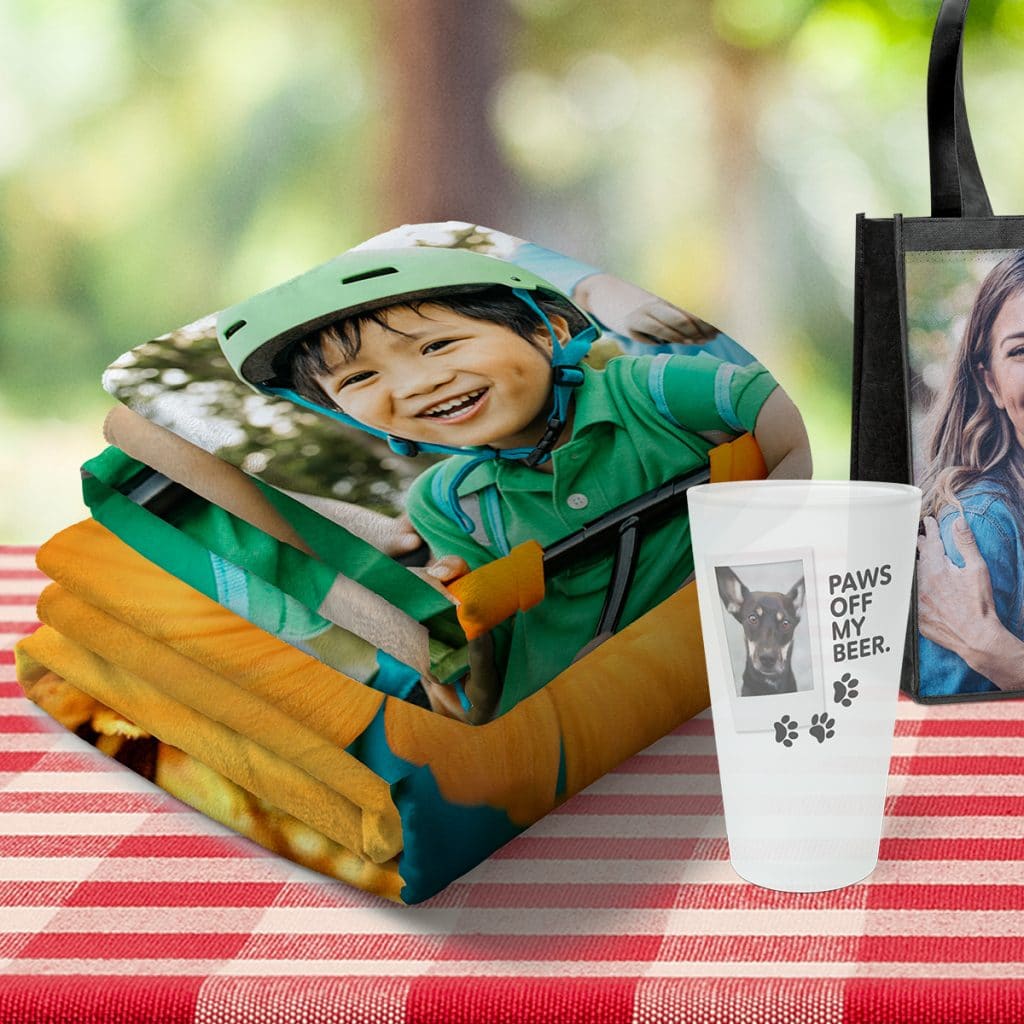 Image of folded photo blanket, pint glass, and tote bag featuring family photos and designs