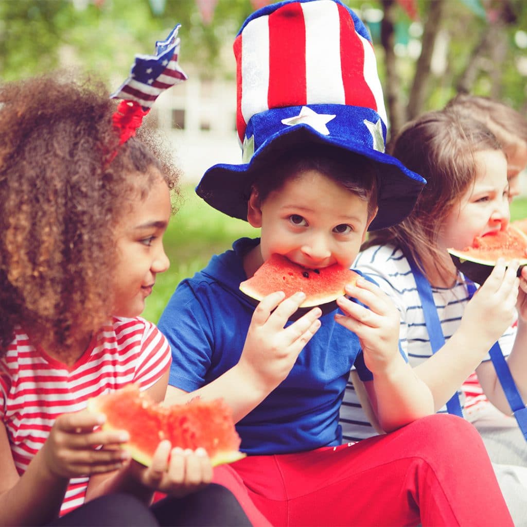 A group of kids wearing red, white, and blue while eating watermelon