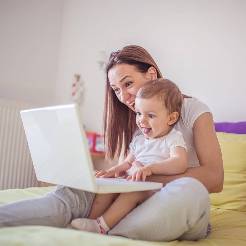 Image of mom and baby holding a white laptop, smiling at the screen