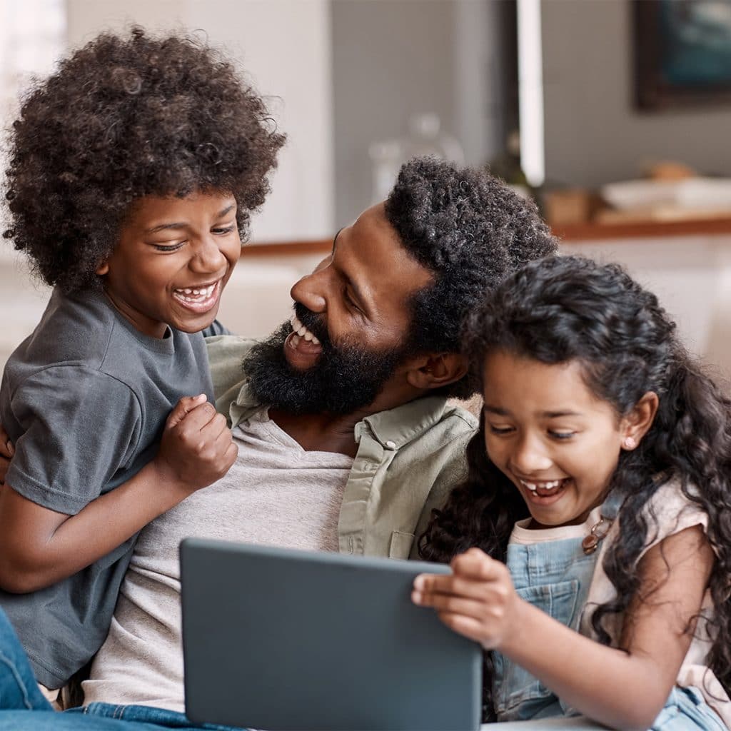 Image of a man, his son, and his daughter smiling and laughing while looking at a tablet