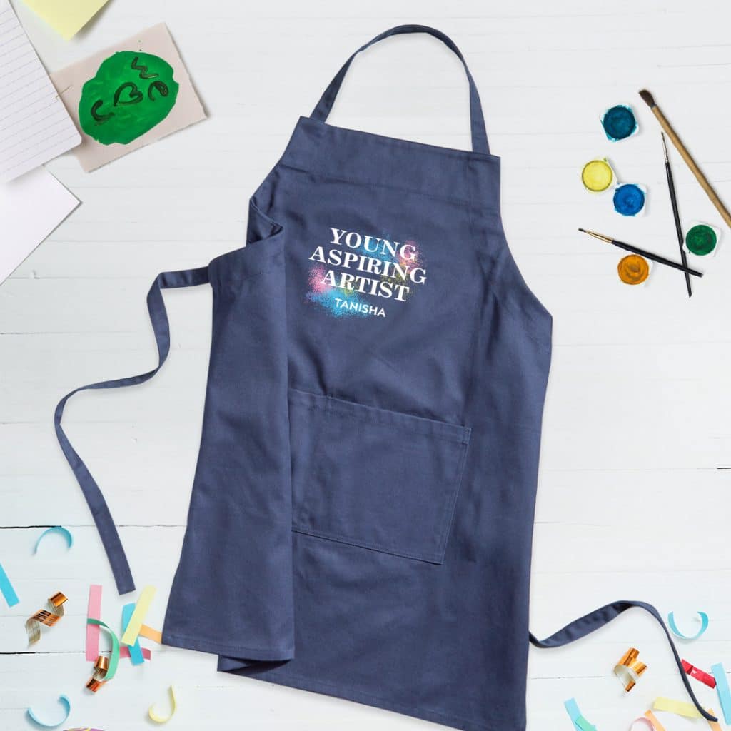 Flat lay image of a navy apron featuring a design that reads "Young Aspiring Artist" and the name Tanisha.