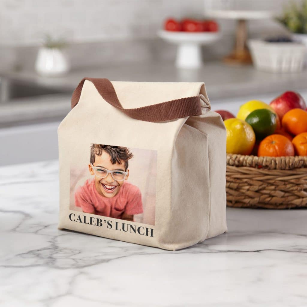 Image of a canvas lunch bag sitting on a countertop featuring a smiling boy and the text "Caleb's Lunch"