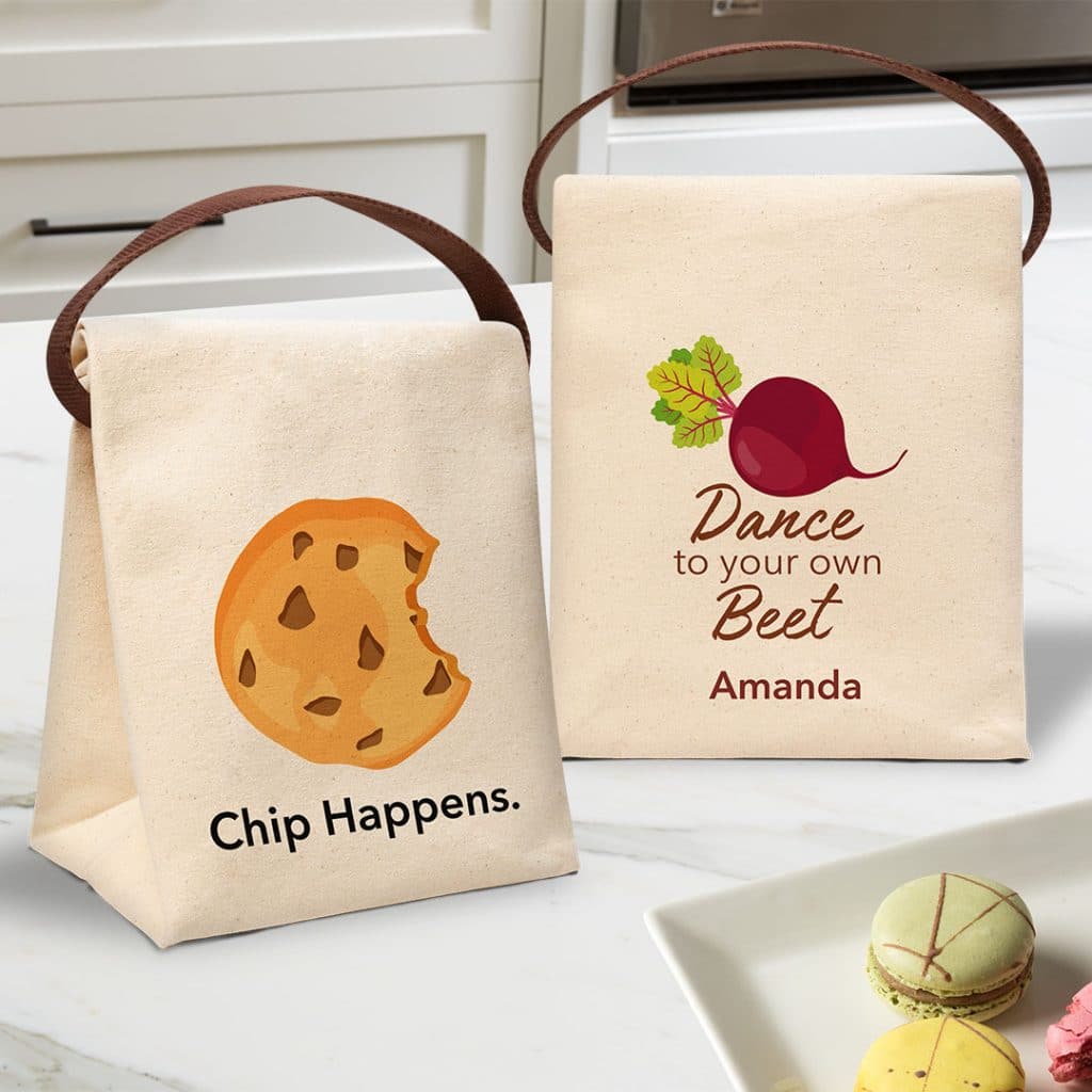 Two lunch bags sitting on a countertop featuring punny food designs.