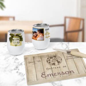 Image of two wine tumblers sitting on a countertop, each featuring wine-centric designs. In front of them is a glass cutting board featuring a wine barrel design