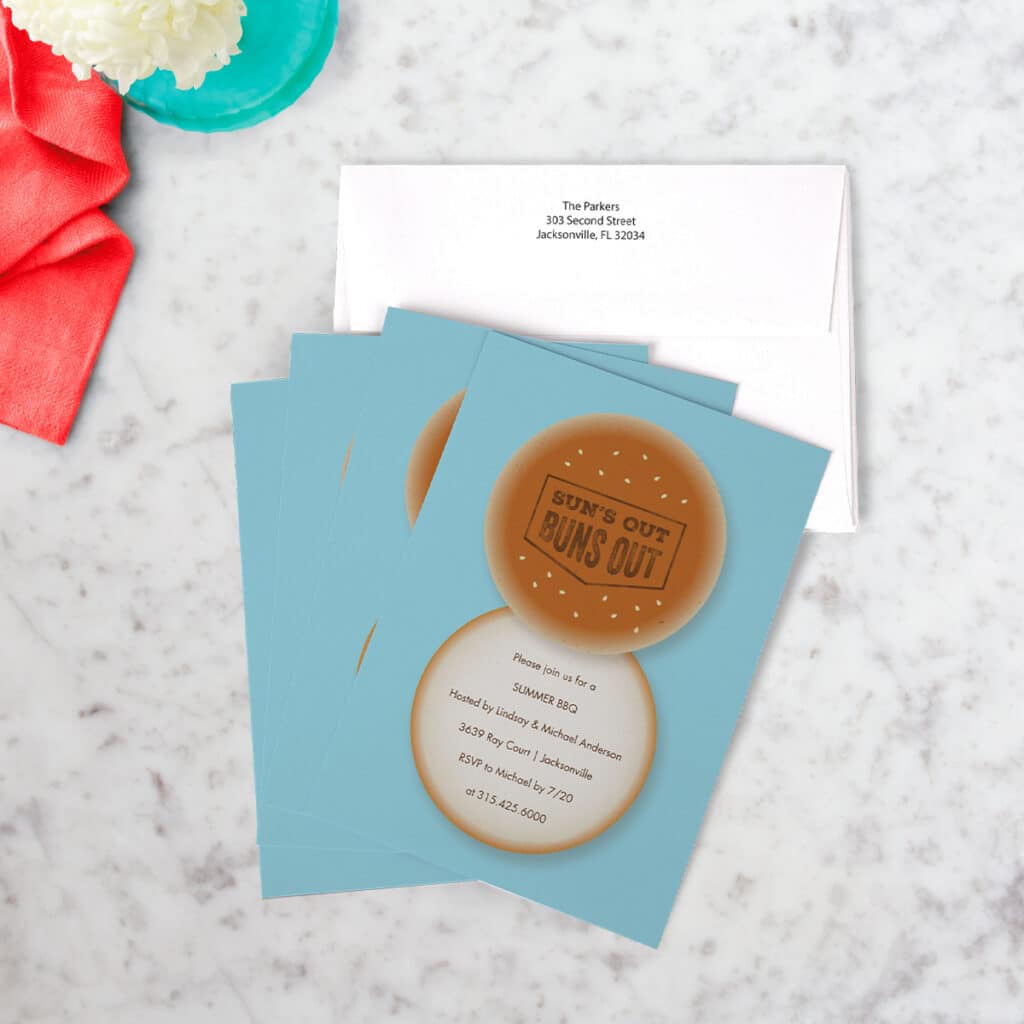 Flat lay image of a card invitation reading "Sun's out, buns out" on a white marble countertop