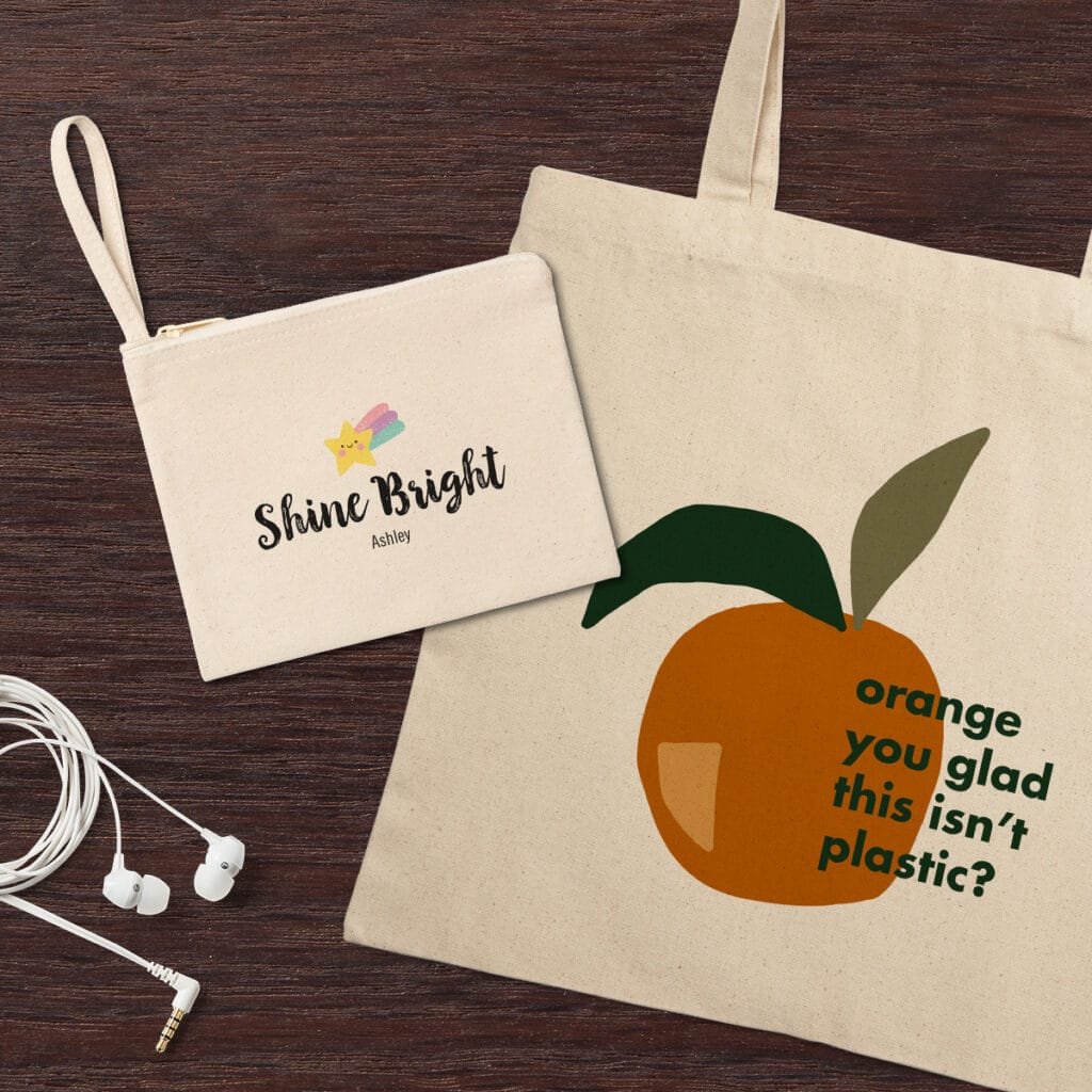 Image of a canvas tote bag and canvas pouch, each with graphic designs and quotes, laying on a tabletop. A pair of headphones lays beside them.