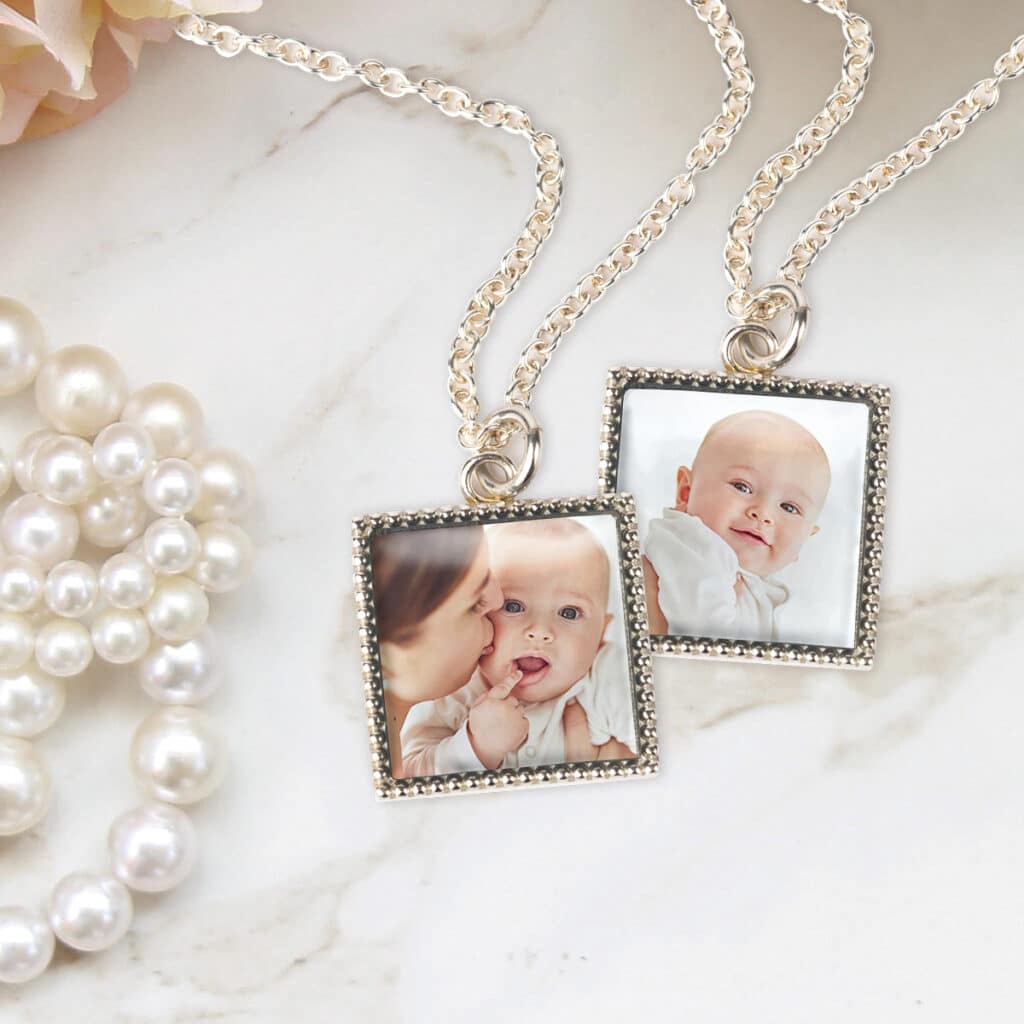 Two photo pendant necklaces laying on a countertop, both featuring a baby and mom. A string of pearls lays beside them.
