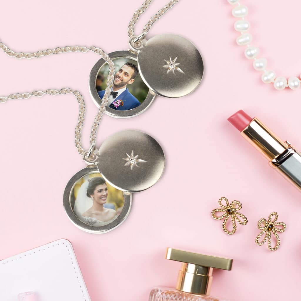 Two photo pendant necklaces laying on a countertop, featuring a bride and groom. A string of pearls, lipstick, a pair of earrings, and perfume lays beside them.