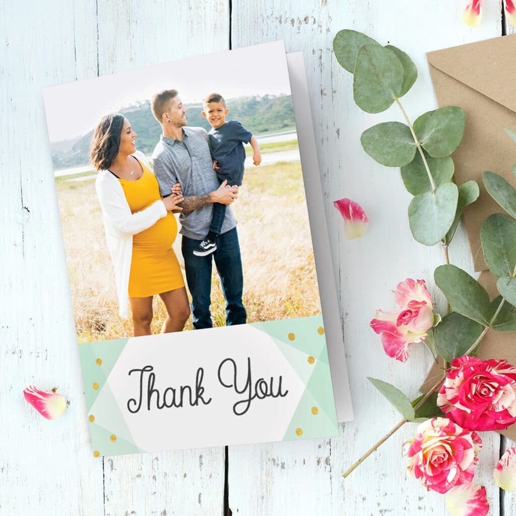 A thank you card with a family image presented on a desk with lovely colourful pink flowers