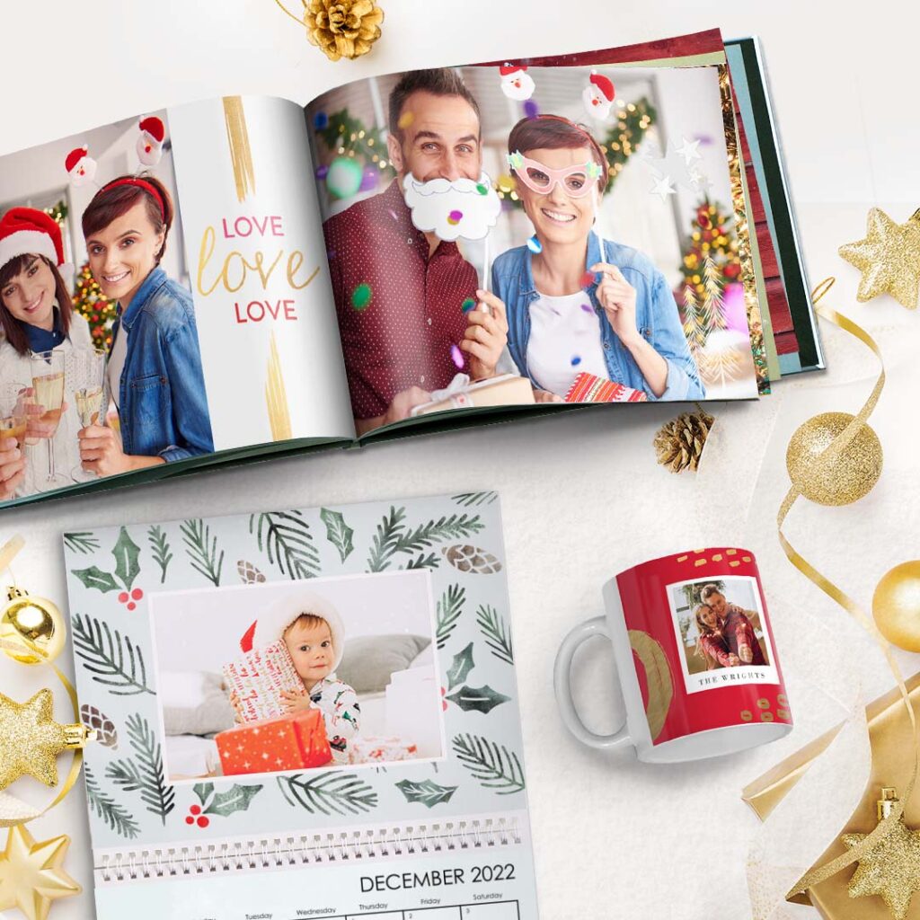 a Christmas photo book, calendar and a mug presented on a surface with golden ornaments and stars